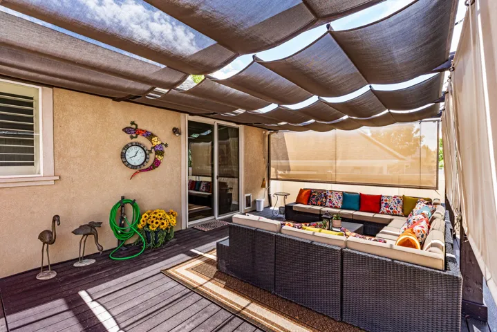 Expansive outdoor living area featuring a covered patio with a retractable shade canopy, wood-finish decking, and direct access to interior spaces through a sliding glass door