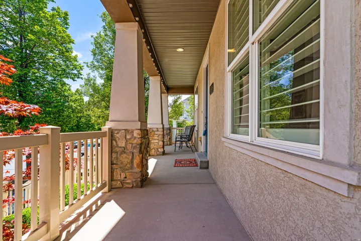 Expansive covered porch featuring stone-wrapped columns, painted balusters, and a textured stucco exterior