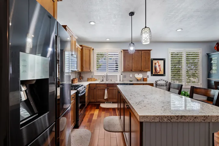 Kitchen featuring stainless steel appliances, wood-finish flooring, wood cabinetry, light-toned countertops, and plantation shutters