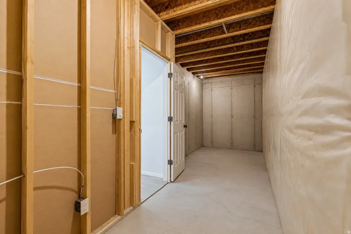 Unfinished basement area featuring exposed wood framing, concrete foundation walls, and insulation