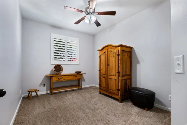 Room featuring neutral gray walls, textured carpet flooring, and a ceiling fan with integrated lighting