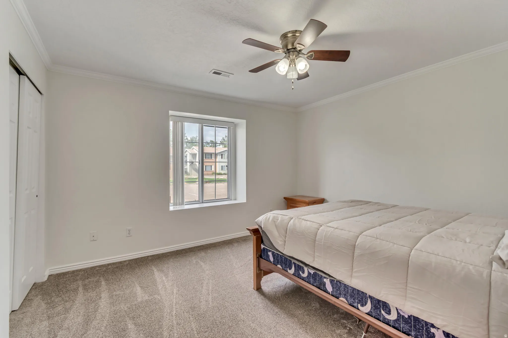 Carpeted interior room featuring a window with blinds, ceiling fan with light fixture, and crown molding