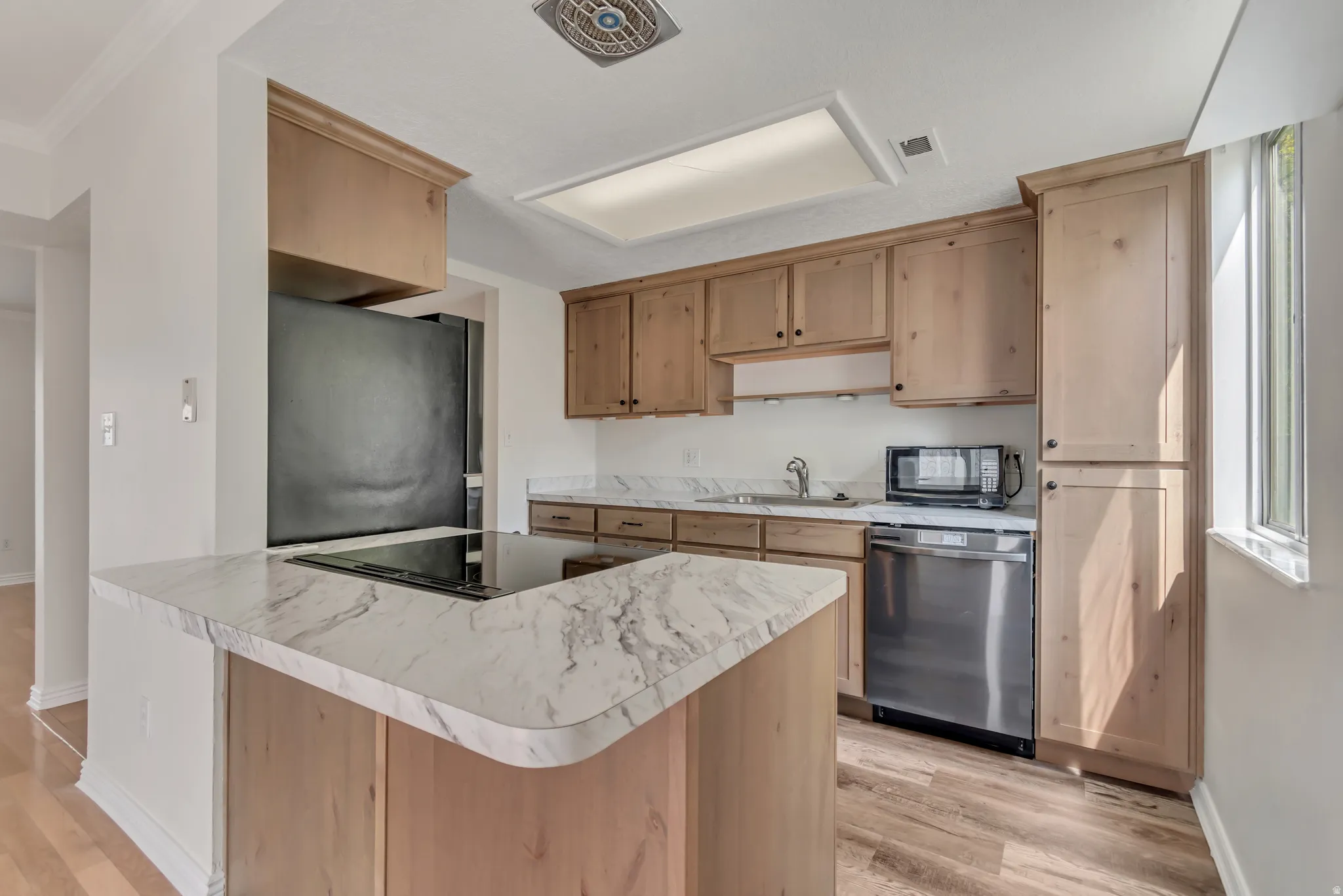 Kitchen featuring wood-finish cabinetry, white countertops with gray veining, a stainless steel dishwasher, a built-in microwave, and wood-finish flooring