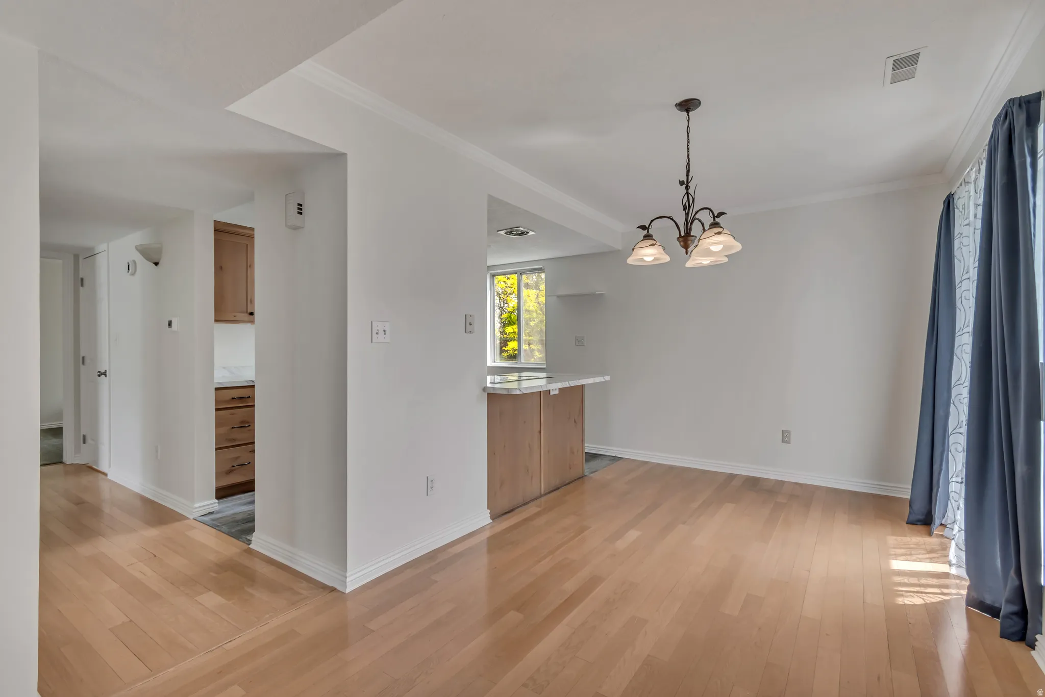 Spacious room featuring wood-finish flooring, white walls, and a multi-light chandelier