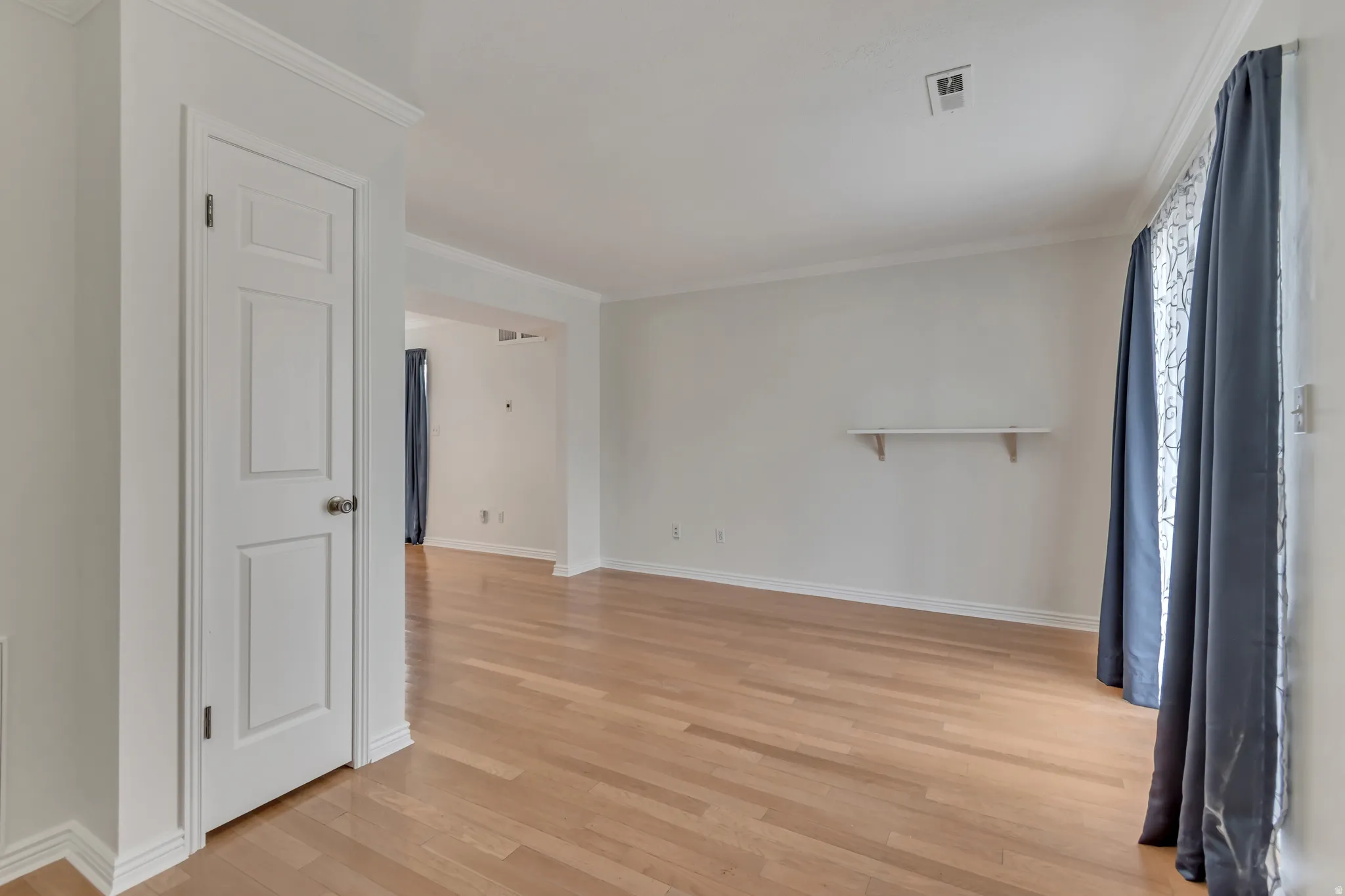 Spacious interior featuring wood-finish flooring, white baseboards, and crown molding