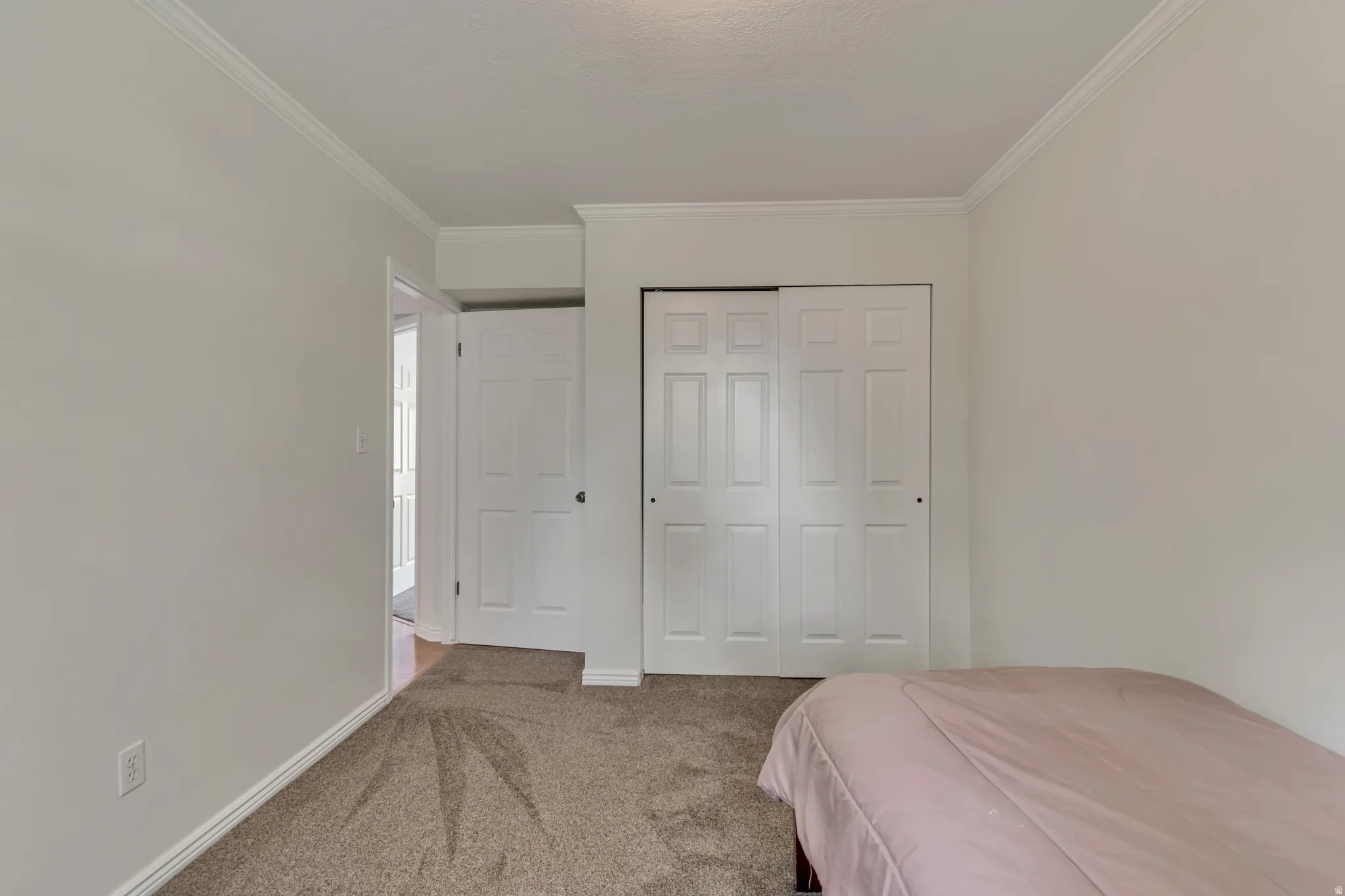 Carpeted bedroom with crown molding, white trim, and a bi-fold closet