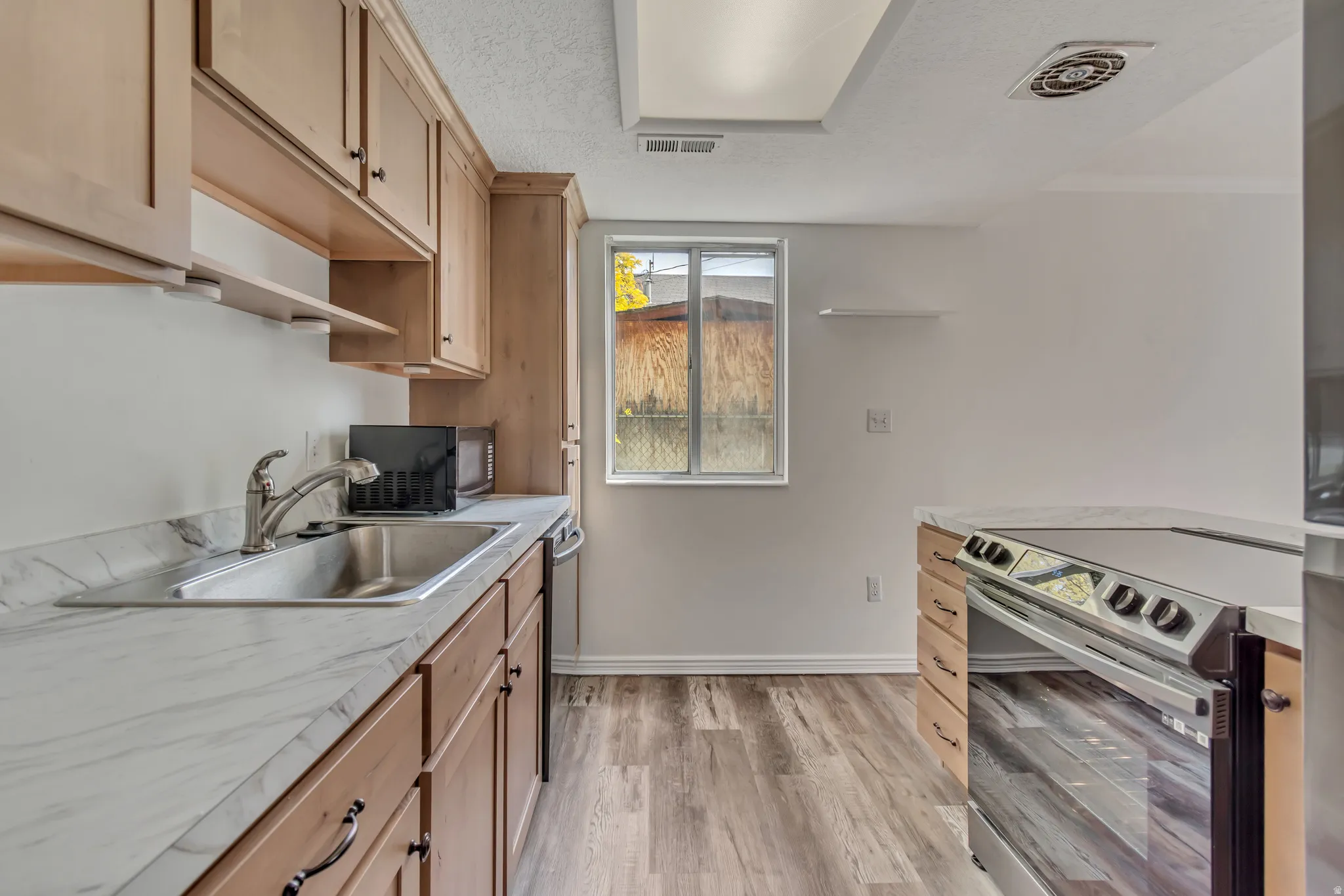 Kitchen featuring wood-finish cabinetry, stainless steel sink, a stainless steel range, light-toned countertops, and wood-finish flooring