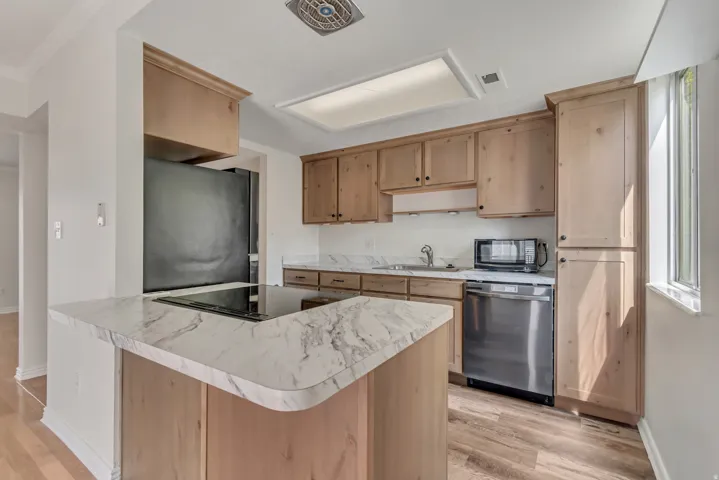 Kitchen featuring wood-finish cabinetry, white countertops with gray veining, a stainless steel dishwasher, a built-in microwave, and wood-finish flooring
