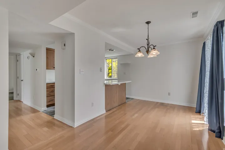 Spacious room featuring wood-finish flooring, white walls, and a multi-light chandelier