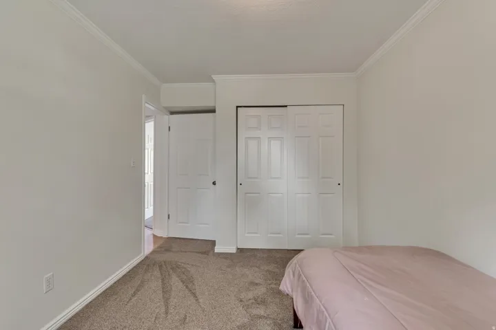 Carpeted bedroom with crown molding, white trim, and a bi-fold closet
