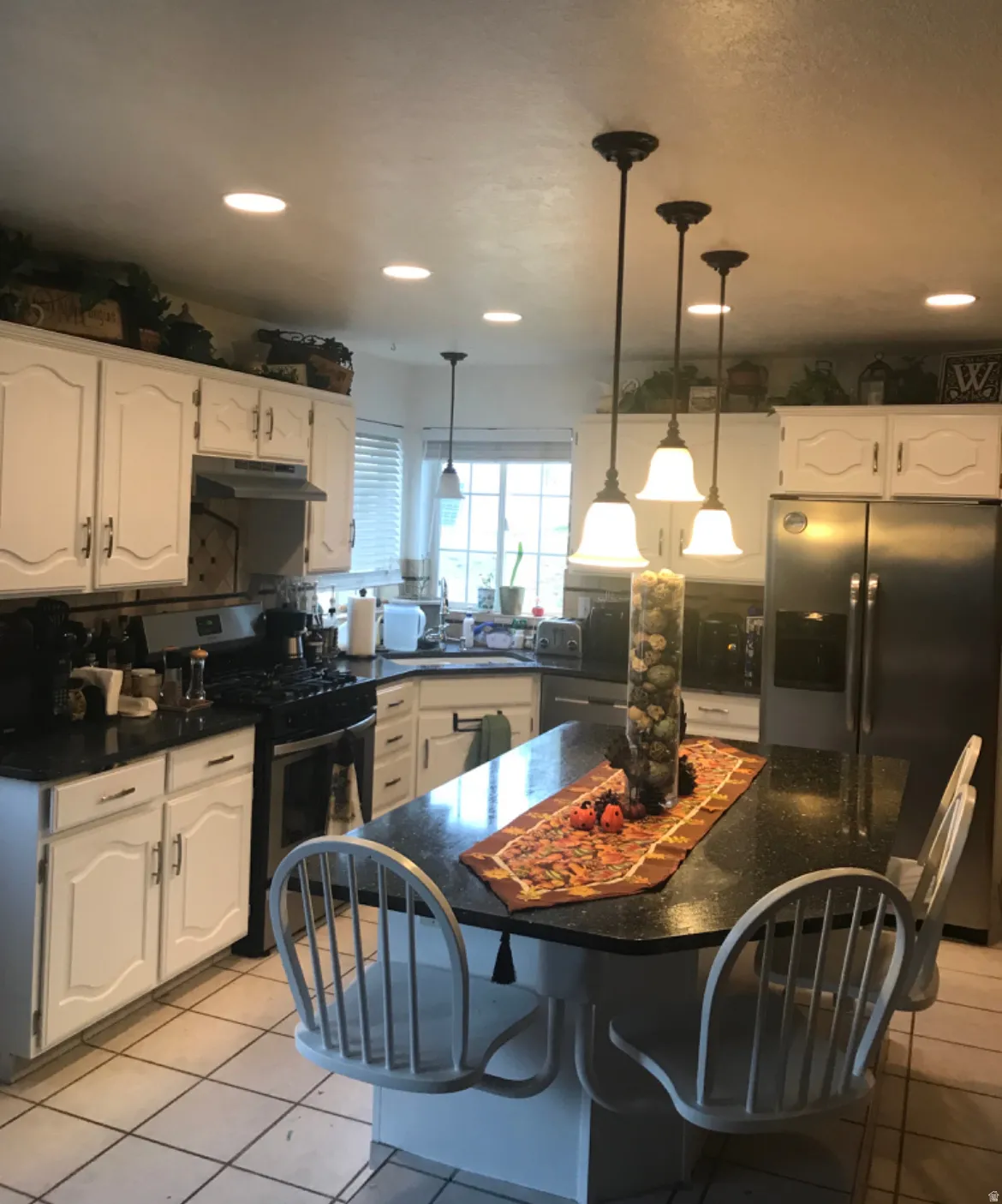 Kitchen featuring white cabinetry, dark countertops, a central island with seating, stainless steel appliances, and recessed lighting