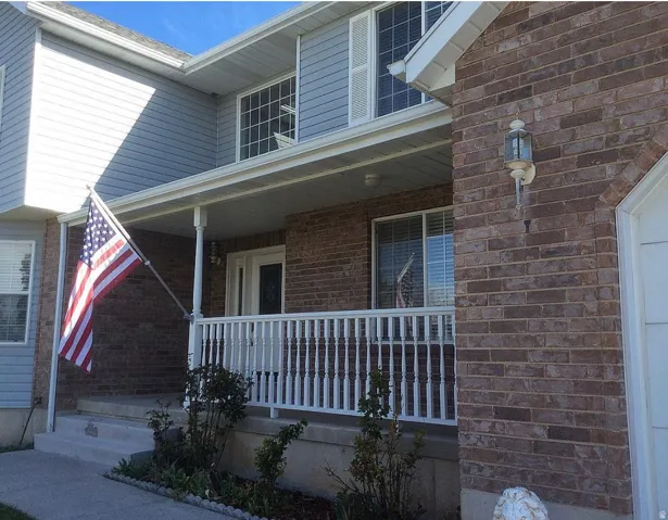 Brick and siding exterior featuring a covered porch, white railing, and decorative outdoor lighting