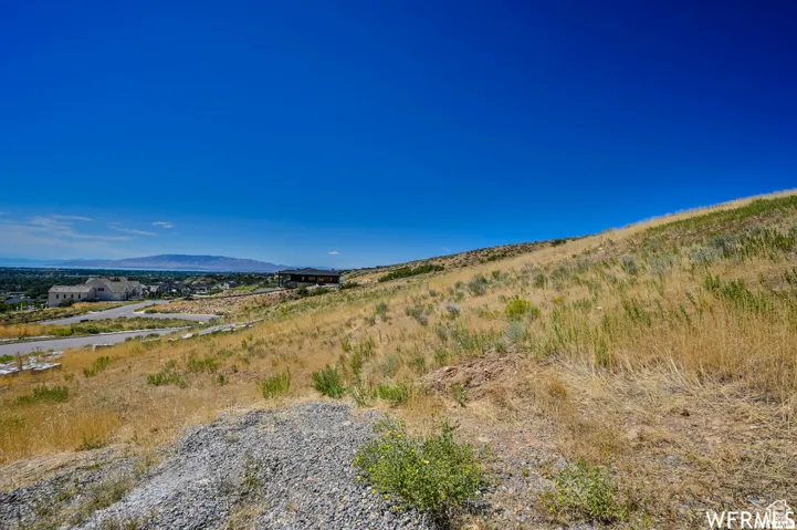 Expansive hillside lot featuring natural vegetation, a clear blue sky, and distant mountain ranges