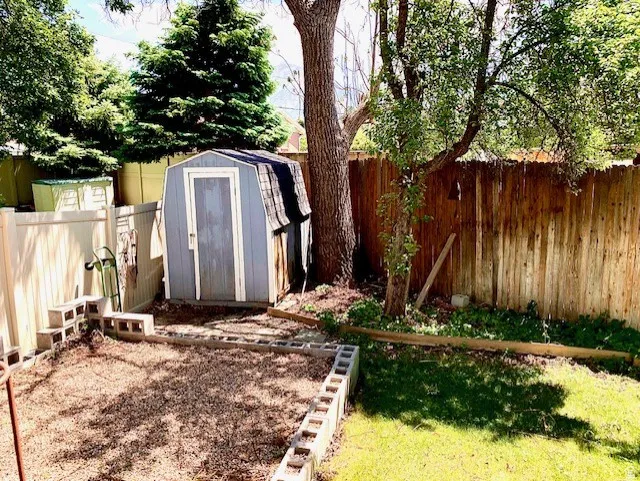 Backyard featuring a blue storage shed with shingle roof, wood privacy fencing, and a vinyl privacy fence