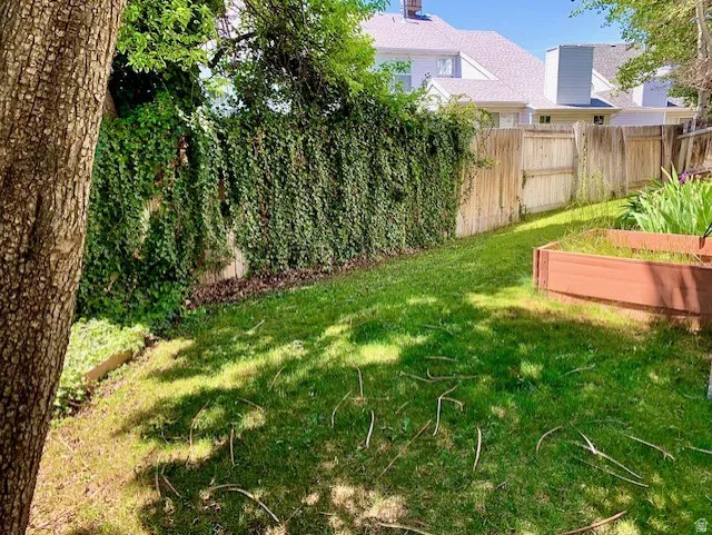 Grassed backyard featuring a mature tree, privacy fencing, and an elevated planting bed