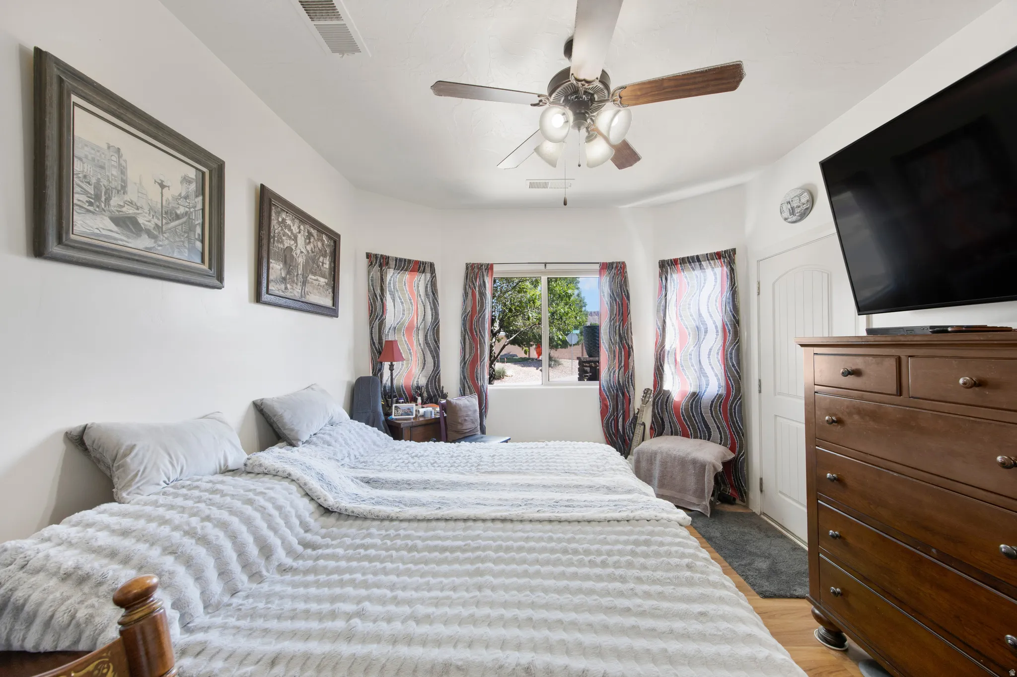 Bedroom featuring wood-finish flooring, a ceiling fan with integrated lighting, and multiple windows with vertical blinds