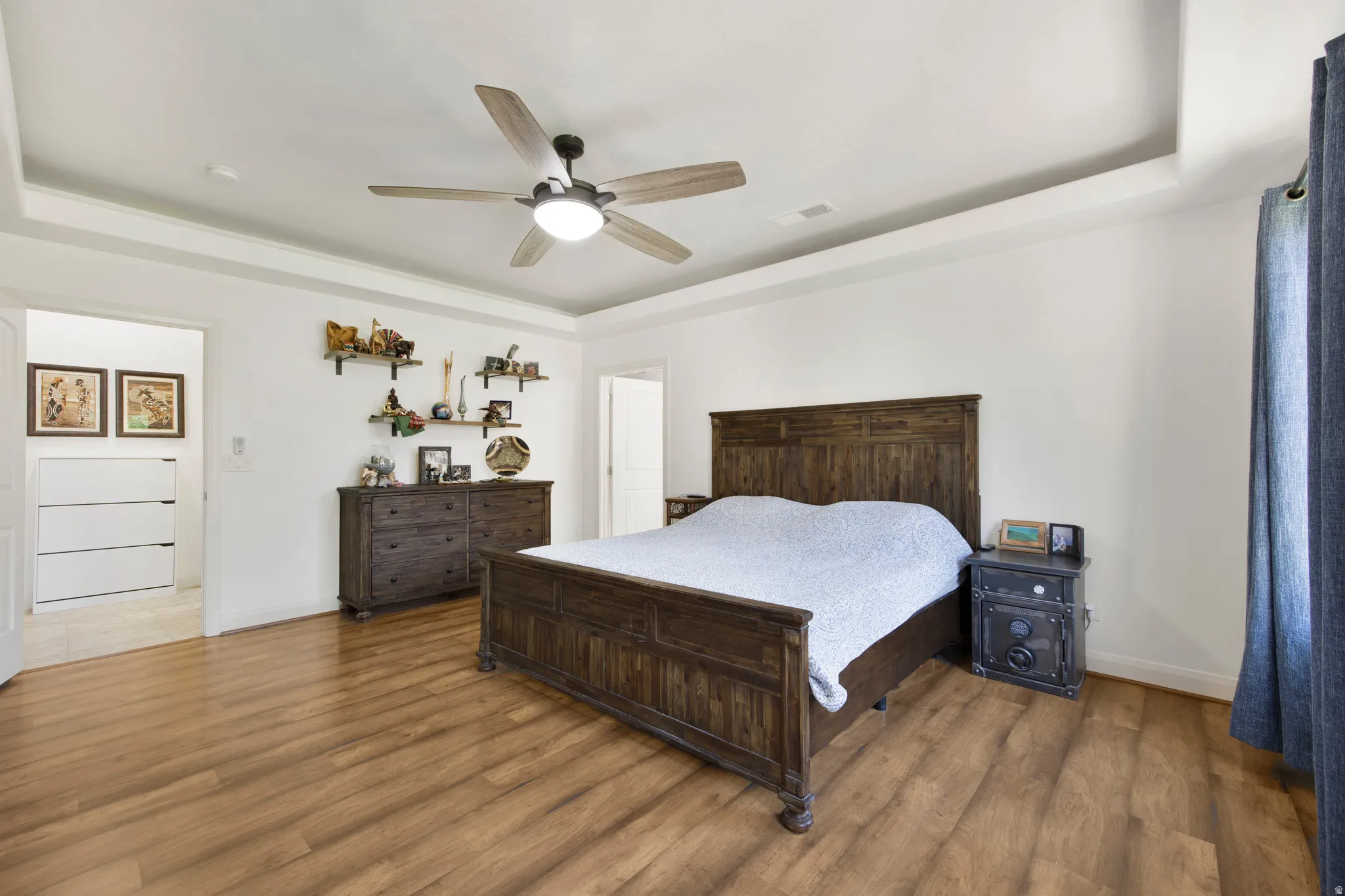 Spacious interior room featuring wood-finish flooring, a tray ceiling, and an overhead ceiling fan with integrated lighting