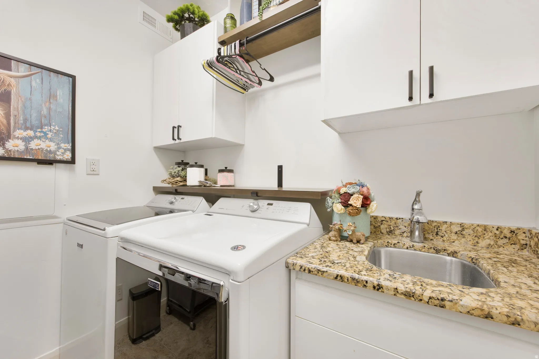 Dedicated laundry space featuring white cabinetry, a built-in utility sink with stone-finish countertop, and an integrated wood-finish shelving unit