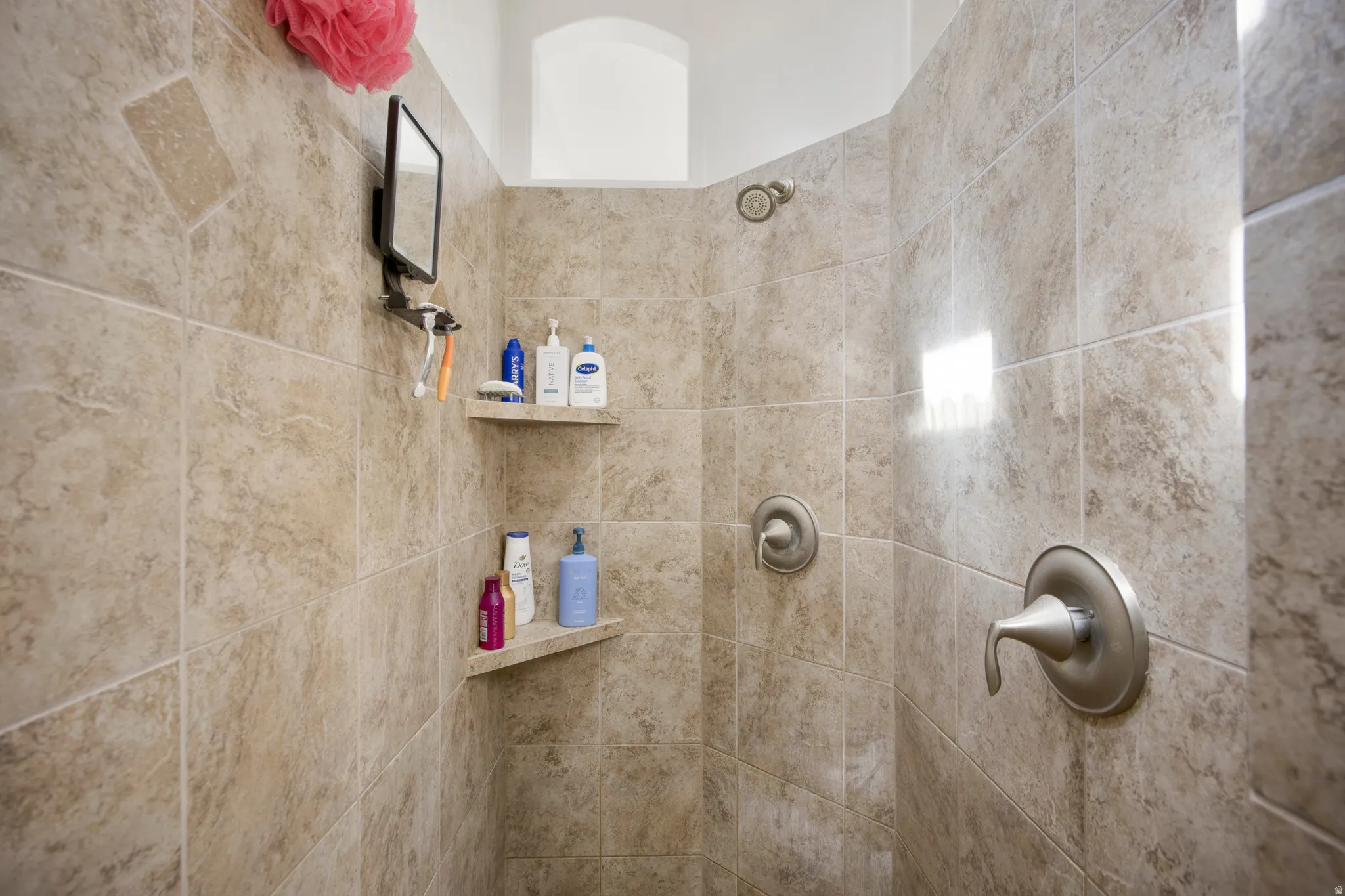 Tiled shower enclosure featuring neutral-toned ceramic tiles, brushed nickel fixtures, built-in corner shelves, and a recessed ceiling niche