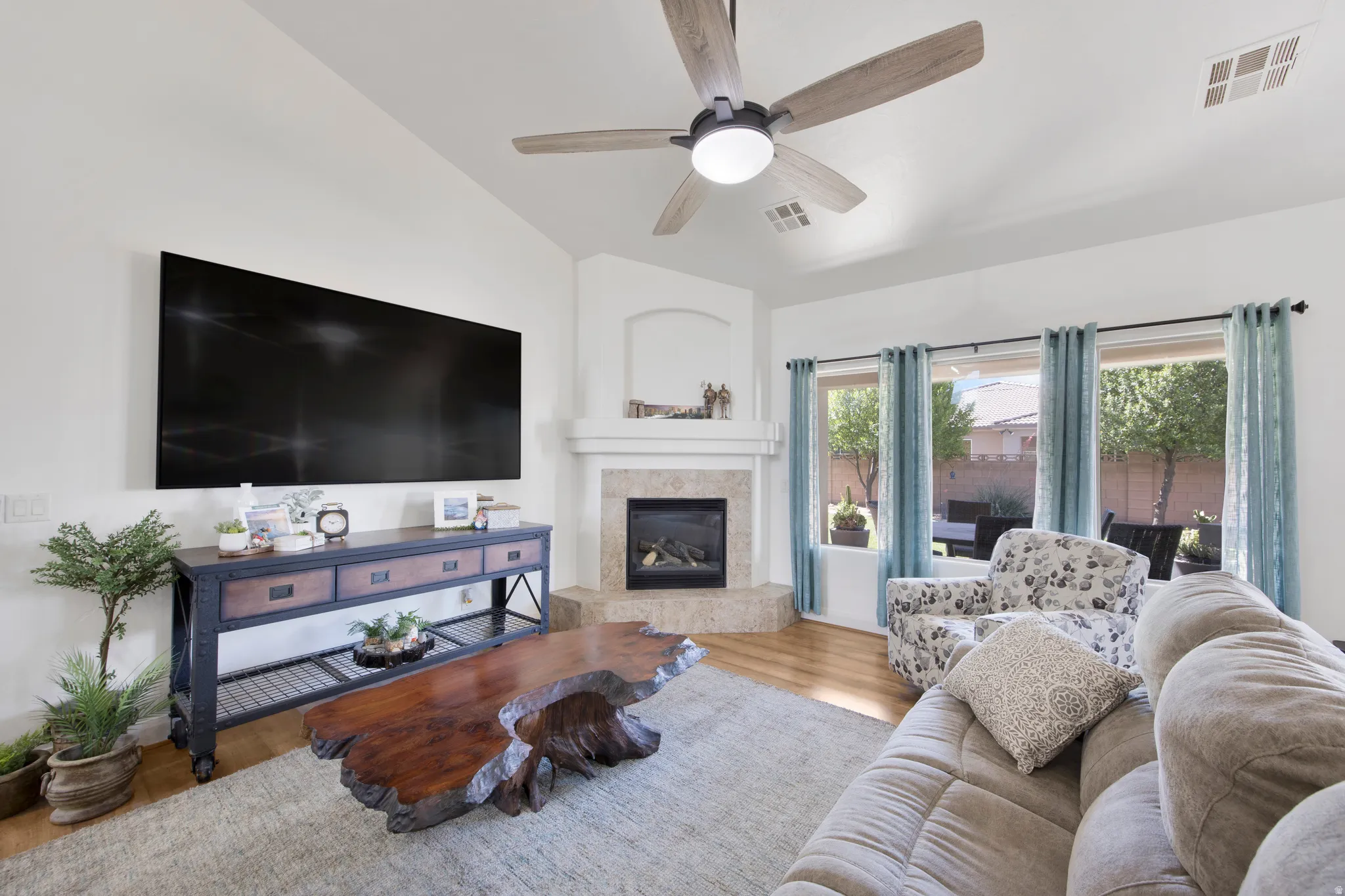 Living area featuring high vaulted ceilings, a contemporary ceiling fan, a gas fireplace with a tile surround, and multiple windows providing natural light