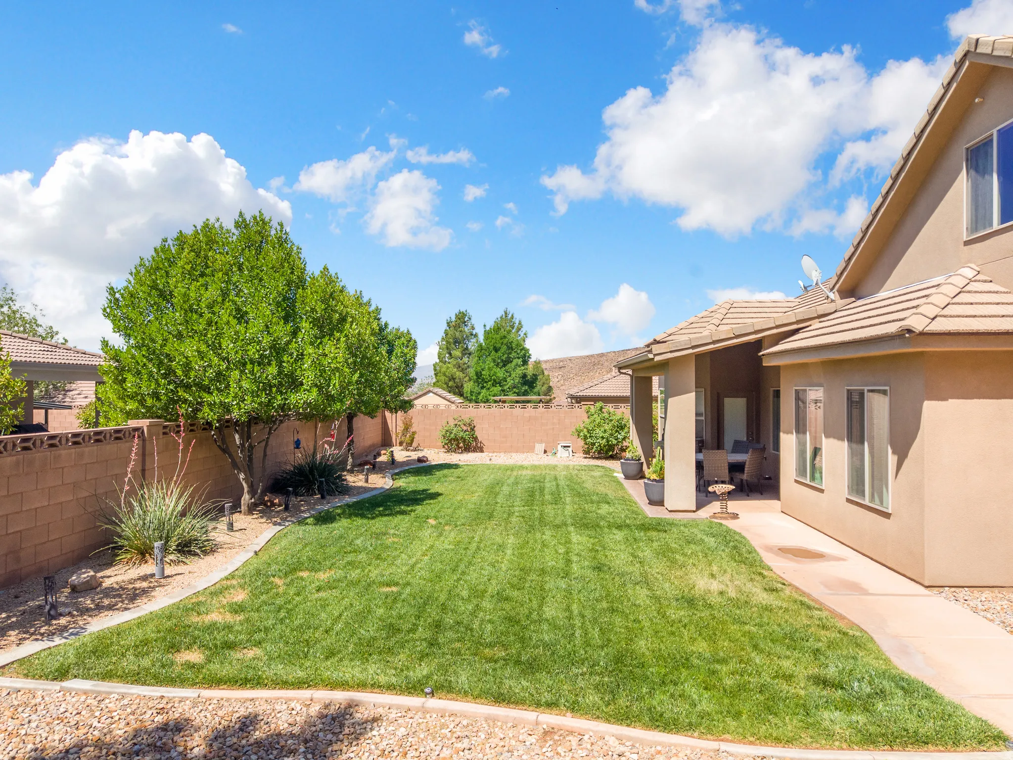 Expansive backyard featuring a large lawn, mature perimeter trees, a covered patio area, and a durable tile roof