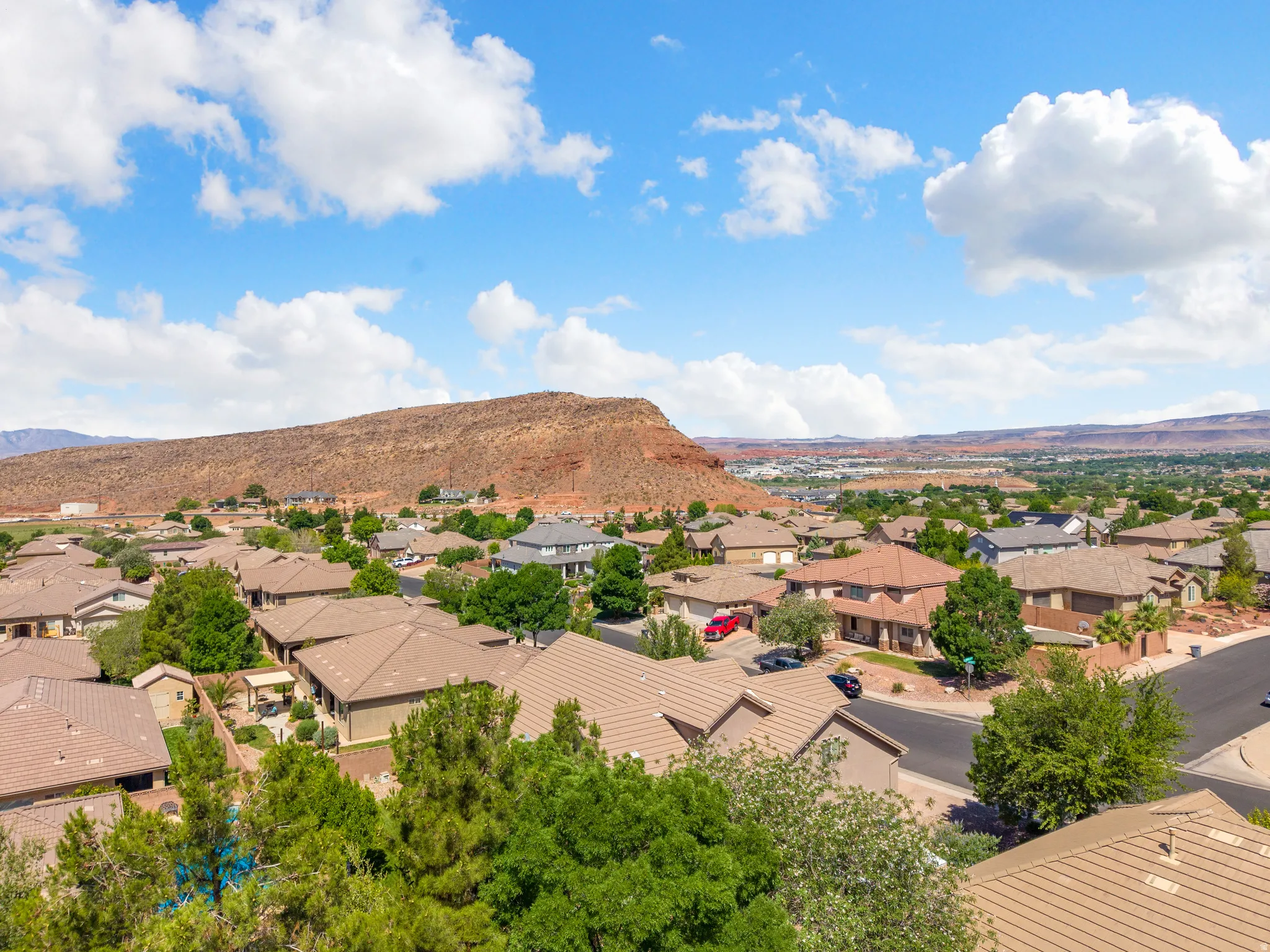 Residential area with varied rooflines and mature trees, set against a prominent red rock mountain backdrop
