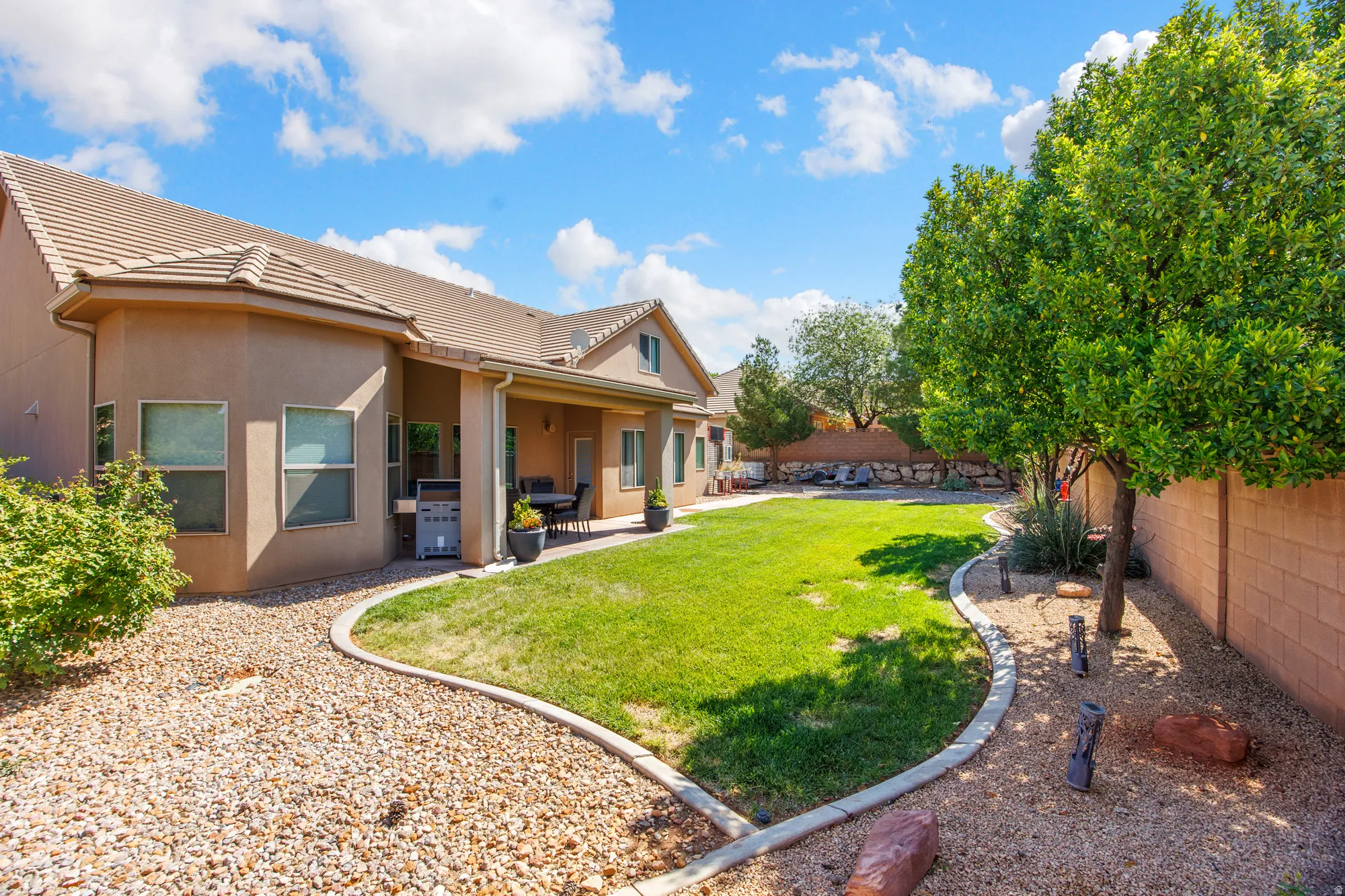 Expansive backyard featuring a lush lawn bordered by decorative rock landscaping