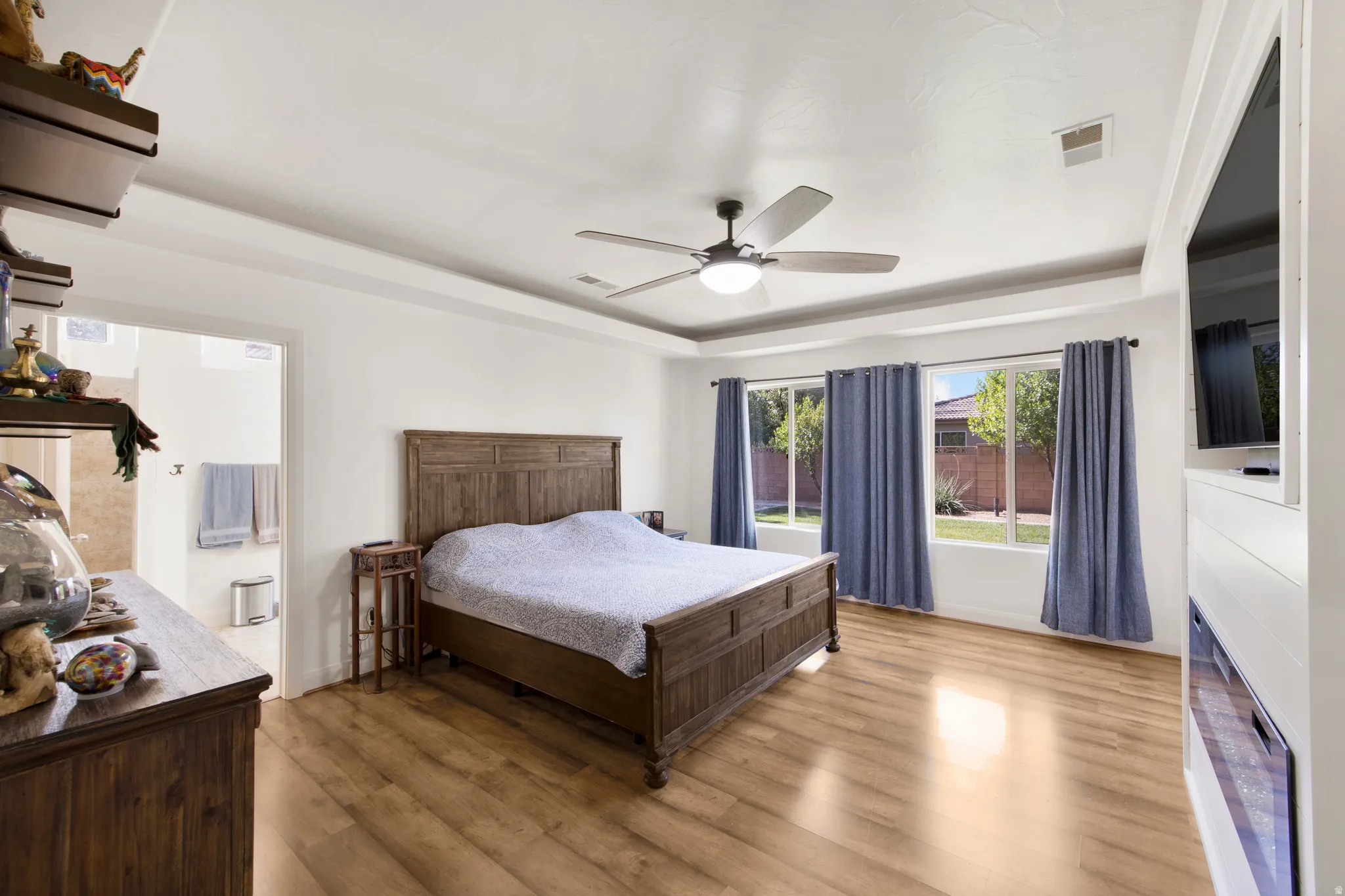 Spacious bedroom featuring wood-finish flooring, a tray ceiling, and a ceiling fan