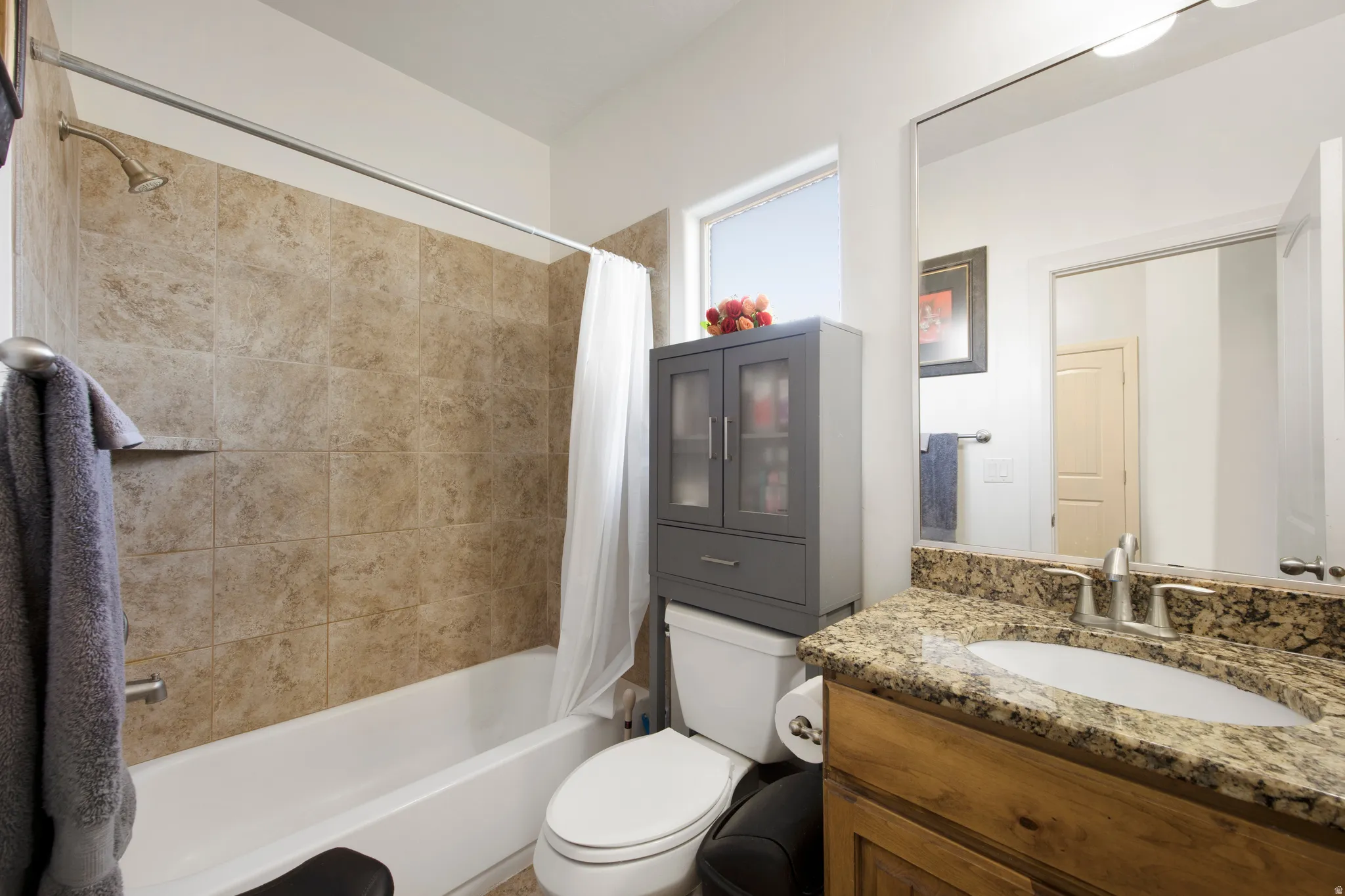 Bathroom featuring a wood-finish vanity with an integrated sink and a speckled countertop, a large wall mirror, and a shower-tub combination with tile surround