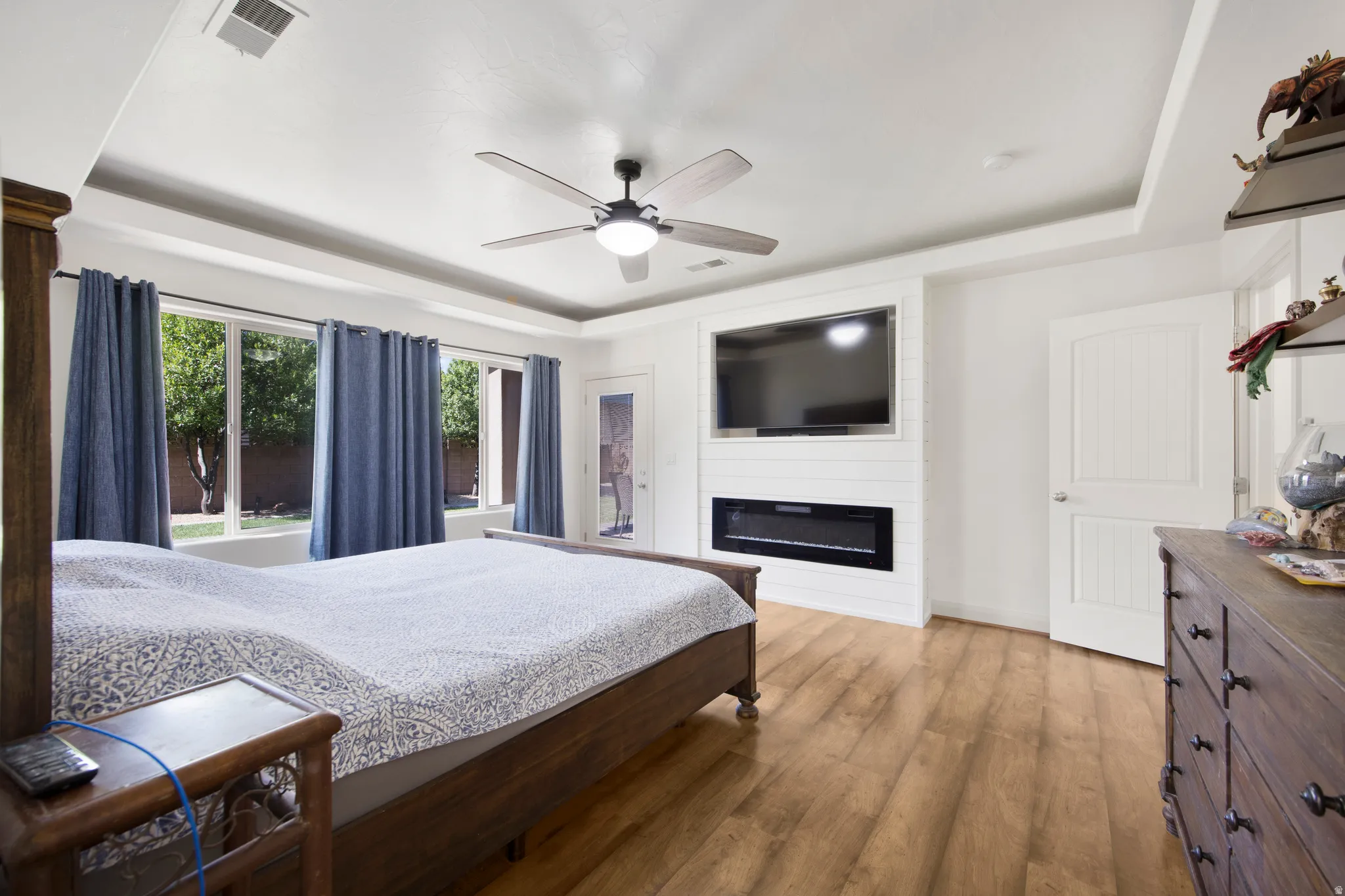 Tray ceiling with ceiling fan, wood-finish flooring, and multiple windows providing outdoor light