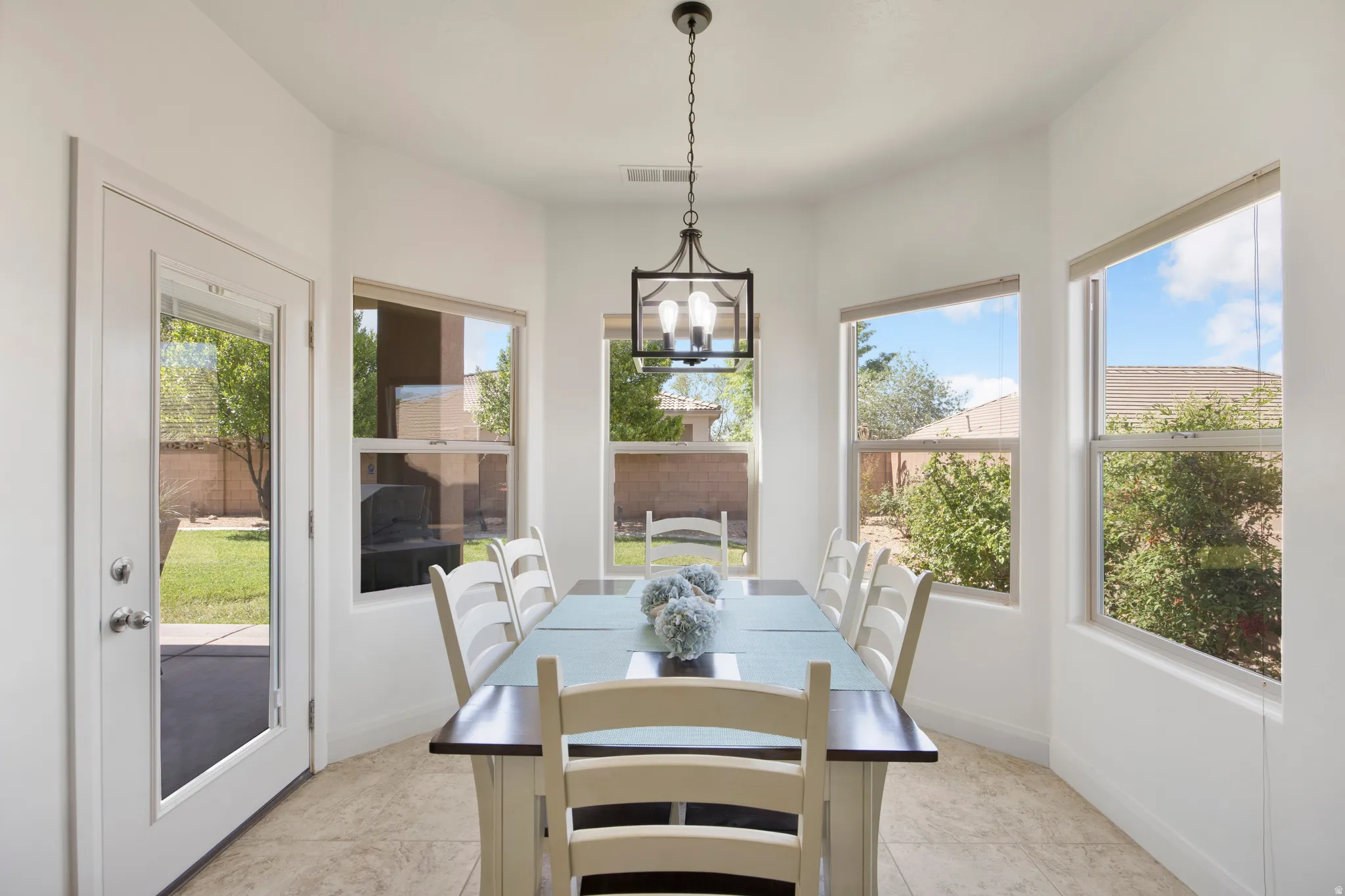 Bright dining area featuring a modern chandelier, bay window design, light-toned tile flooring, and a glass-paneled exterior door