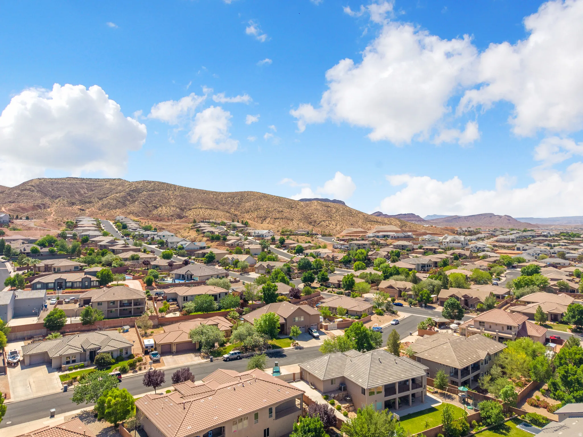 Residential neighborhood with varied architectural styles and mature landscaping, framed by desert hills and a blue sky with scattered clouds