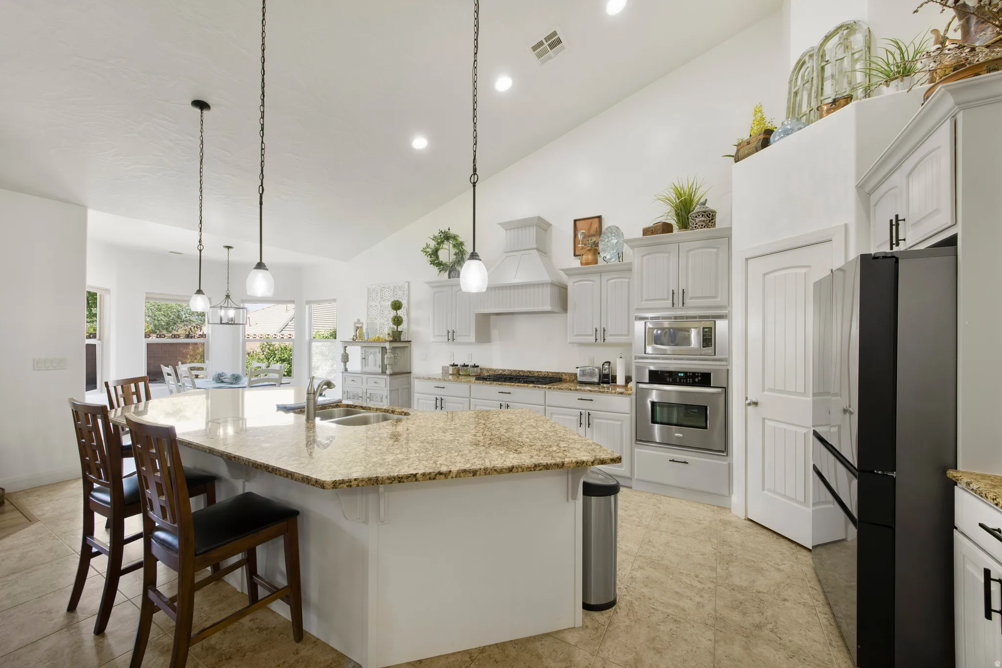 Spacious kitchen featuring a large island with a stone-finish countertop, light-toned cabinetry, stainless steel built-in appliances, recessed lighting, and pendant lighting fixtures