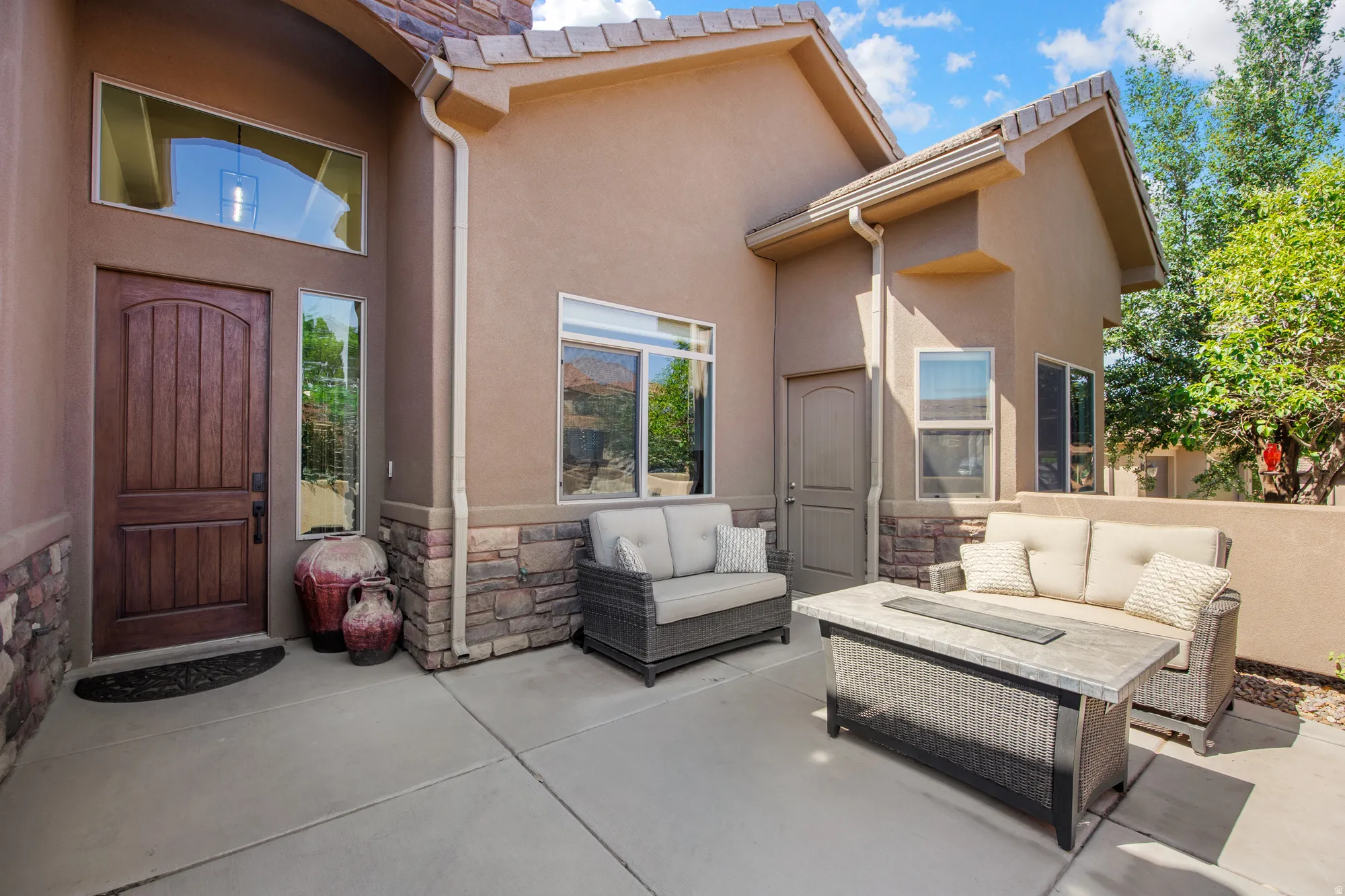 Inviting front patio featuring concrete flooring and a textured stucco exterior with stacked stone accents