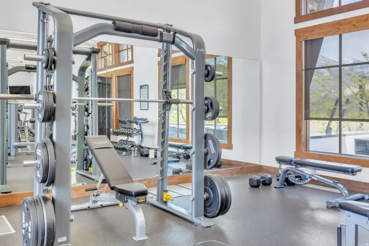 Dedicated fitness room featuring rubber flooring, a mirrored wall, and large windows with natural wood trim