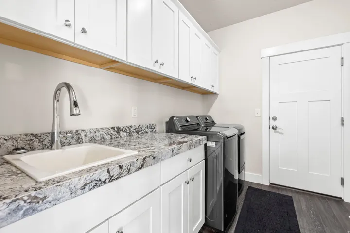 Utility room featuring a built-in sink, stone-finish countertop, white cabinetry with silver hardware, and wood-finish flooring