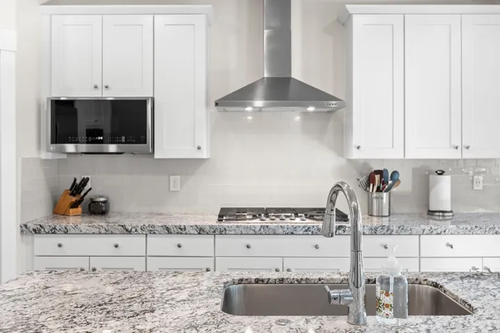Kitchen featuring granite countertops, white shaker-style cabinetry, a stainless steel gas range, an undermount sink with a gooseneck faucet, and a subway tile backsplash