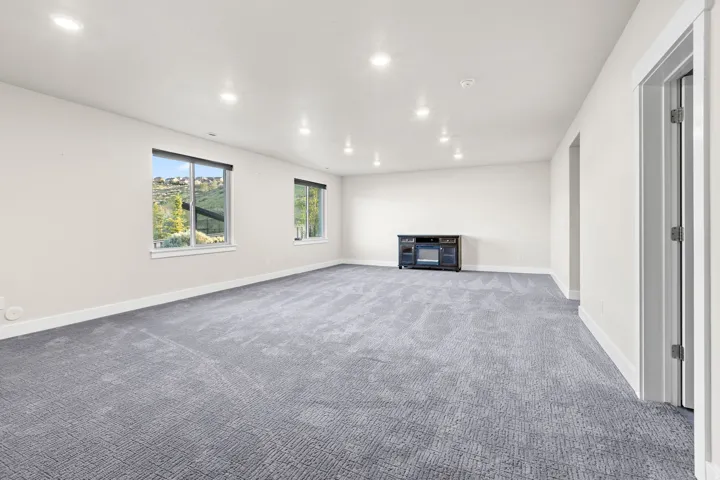 Spacious room featuring neutral-toned walls, recessed lighting, two windows, and patterned carpeting