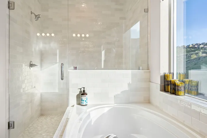 Contemporary bathroom featuring a built-in soaking tub, a clear glass enclosed shower, and a large window overlooking a distant hillside