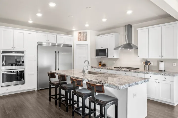 Expansive kitchen featuring a large island with seating, stainless steel appliances, white shaker cabinetry, and wood-finish flooring