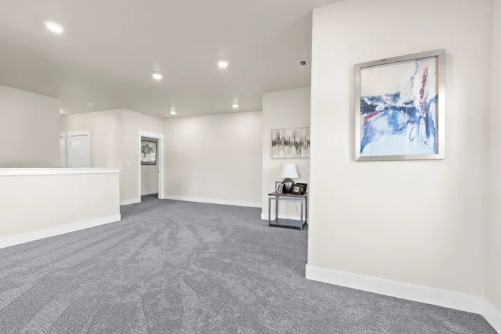 Spacious room featuring gray patterned carpeting, recessed ceiling lighting, and a neutral wall color with white baseboards