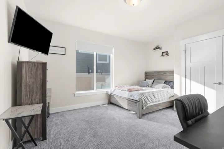 Bright living space featuring a window with roller shade, neutral wall paint, and light gray carpet flooring