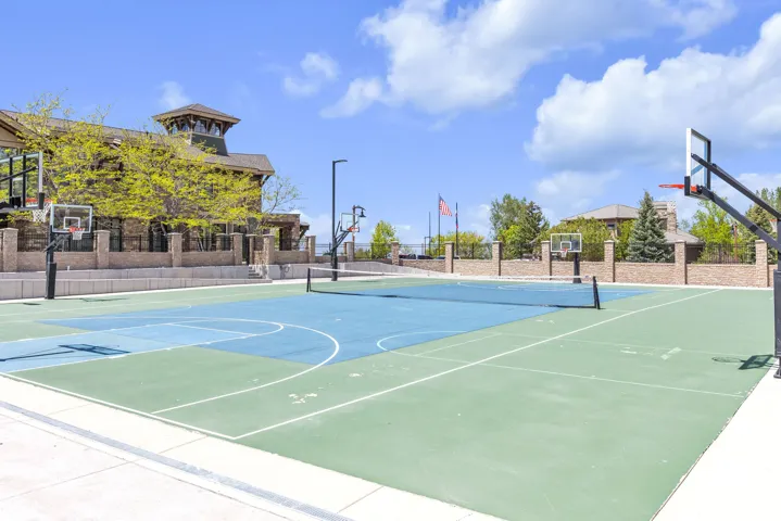 Multipurpose sports court featuring two basketball hoops, a tennis net, and distinct green and blue playing surfaces