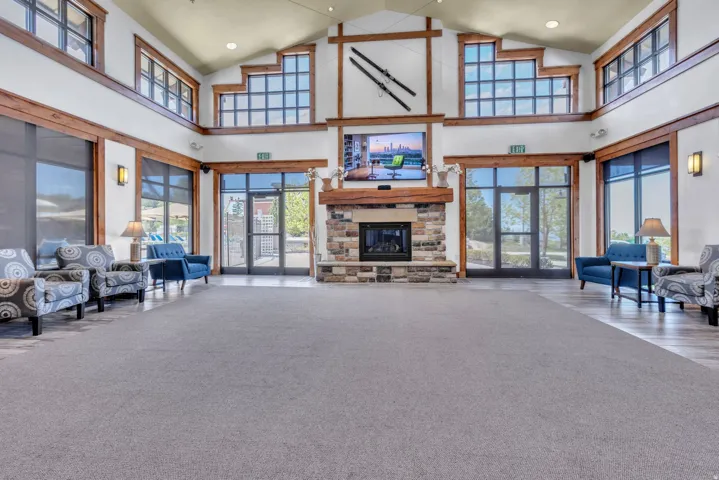 Spacious common area featuring a stone fireplace with a wood mantle, high vaulted ceilings, expansive window walls, and durable carpet and wood-finish flooring