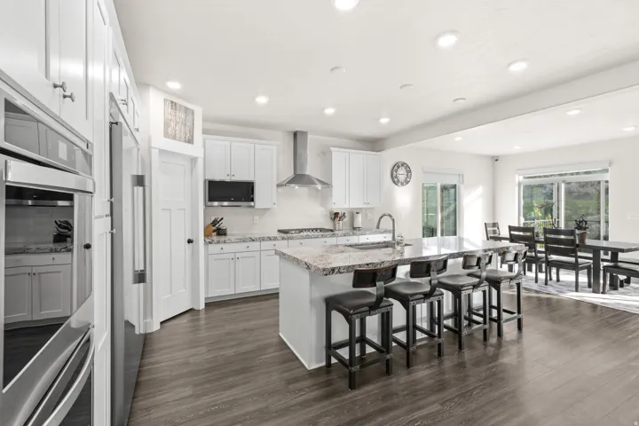 Spacious kitchen featuring an expansive center island with seating, stainless steel appliances, white cabinetry, and wood-finish flooring