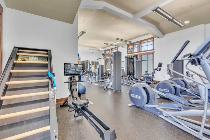 Fitness center featuring high ceilings with exposed beams, large windows, and robust exercise equipment