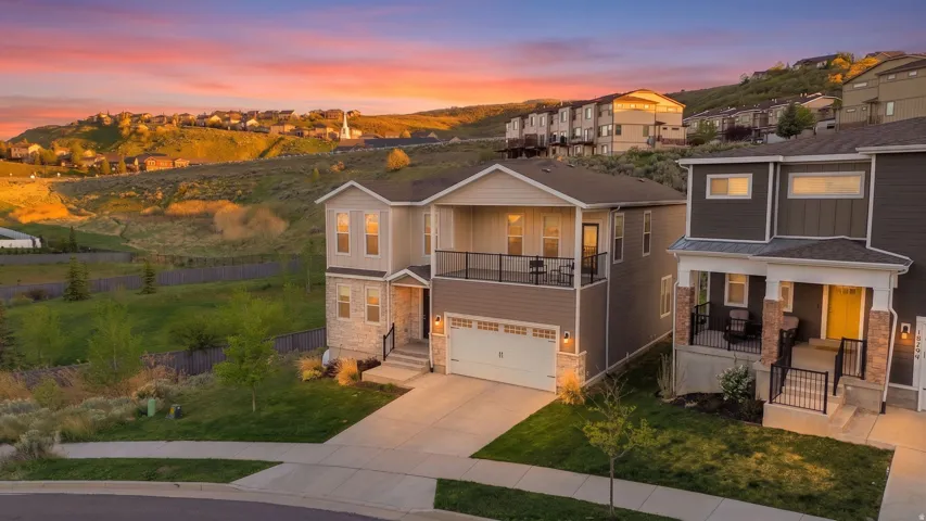 Modern two-story residence featuring a two-car garage, stone and siding exterior, and an upper-level balcony