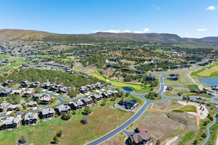 Hilly landscape with scattered residences, paved roads, and green golf courses featuring water elements