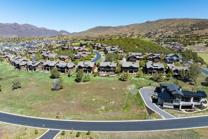 Expansive residential development with contemporary homes, winding paved roads, and lush green landscaping, set against a mountainous backdrop