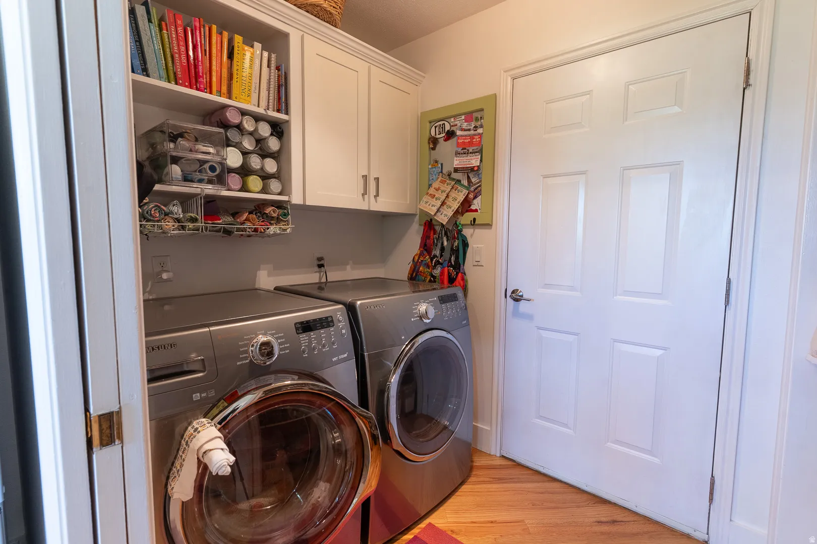 Laundry area featuring built-in cabinetry, open shelving, and wood-finish flooring inside the garage door